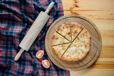 Tahtada ev yapımı pizza, merdane ve domates.