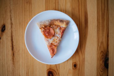 Tahta bir masada beyaz bir tabakta bir dilim pizza var.