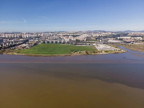 Aerial view of a garden park facing the Tagus river next the Vasco da Gama bridge with Trancao river and Lisbon residential district skyline in background, Portugal.