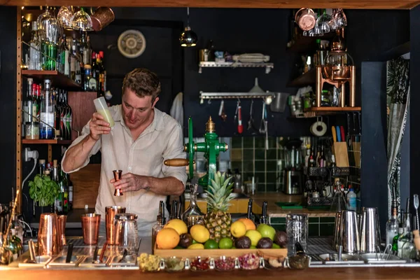 View of a young man in elegant shirt working as professional bartender pouring alcohol in a measuring cup using a shaker, Lisbon, Portugal.