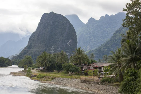 Evler ve dağlar sahil Nam şarkı nehir Vang Vieng boyunca Laos bulunur.
