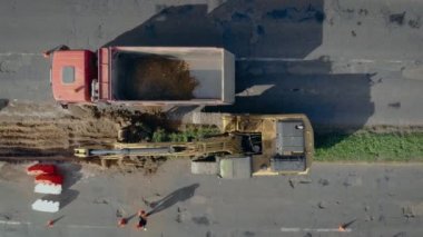 Büyük sürüngen kazıcısı toprak kazıyor ve yoldaki çöp kamyonuna yüklüyor.