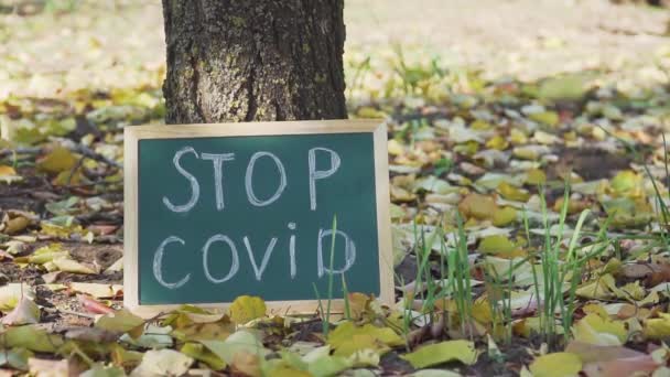 Znamení s nápisem stop covid stojící pod stromem ve světě bez lidí a žluté listy padají na podzim — Stock video