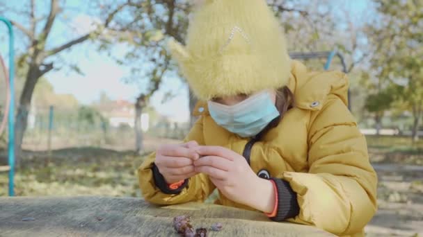 Klein meisje in medisch gezichtsmasker spelen alleen op kinderen speeltuin en houden in haar hand wat fruit — Stockvideo