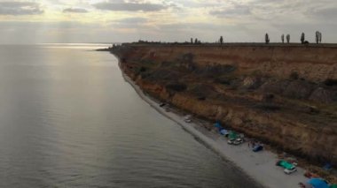 Batan güneş ışınları, deniz kıyısında gezgin gezginlerle birlikte bulutları delip geçiyor.