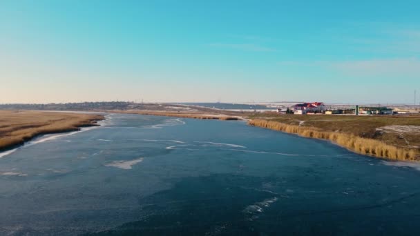 Зимний пейзаж с замерзшей водой в реке и зданиями далеко под голубым небом — стоковое видео