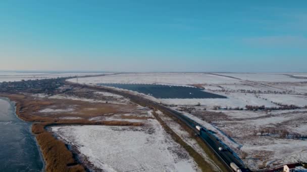 Зимнее шоссе с движущимися грузовиками возле солнечных панелей Стантон и снег на холмах — стоковое видео