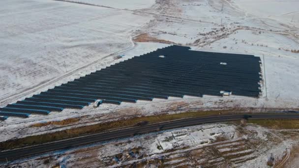 Horní pohled na moderní solární panely stanice se nachází na poli se sněhem v blízkosti silnice s pohybujícími se vozidly v zimě — Stock video