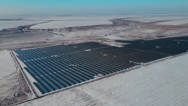 Yüzlerce mavi güneş paneli, kışın karlı tepeler ve tarlalar arasındaki büyük güneş çiftliğinde. — Stok video