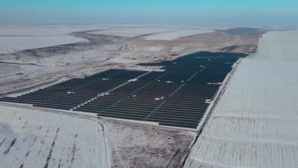 Gran granja solar de paneles solares azules entre campos y colinas con nieve en invierno — Vídeos de Stock