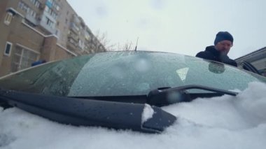 Adam arabanın kapısını açar içeride oturur ve cam silecekleri ile düşen ve eriyen karları siler.