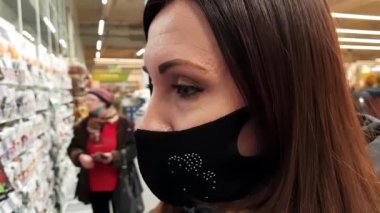 Koruyucu antivirüs maskesi takan kadın müşteri, mağazadan satın almak için gerekli malzemeleri seçiyor