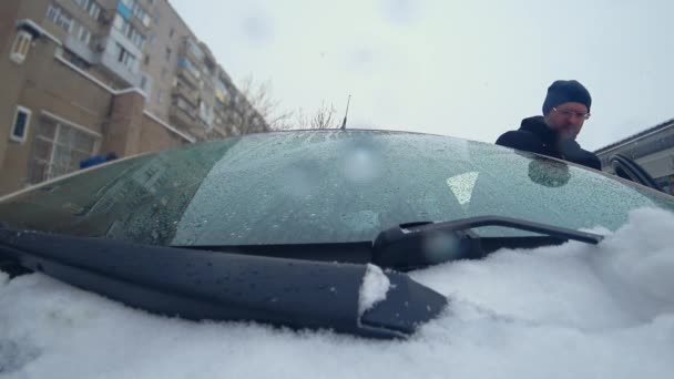 Mann öffnet Autotür und wischt Windschutzscheibe mit Scheibenwischer von herabfallendem und schmelzendem Schnee — Stockvideo