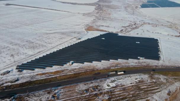 Stazione di celle solari in campo innevato vicino autostrada con camion pesanti in movimento in inverno — Video Stock