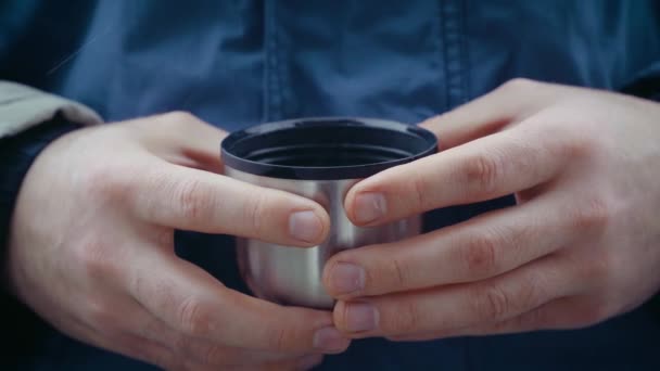 Κοντινό πλάνο των χεριών του τουρίστα ταξιδιώτη με μεταλλική κούπα. Πεζοπόρος άνθρωπος με θερμό φλιτζάνι τσάι ή καφέ σε χιονοθύελλα σε ουδέτερο φόντο — Αρχείο Βίντεο