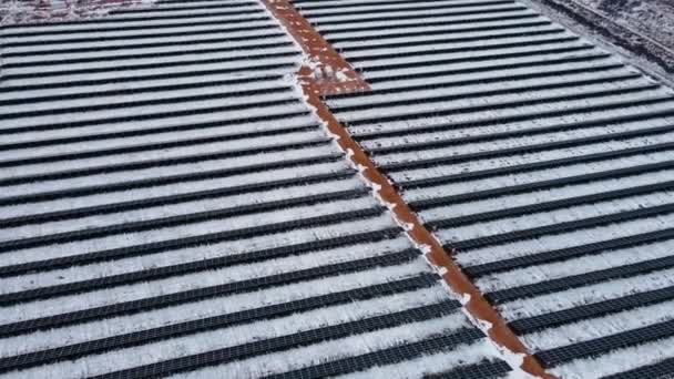 Filmische Luftaufnahme von oben nach unten auf grafisch geraden Linien von Solarzellen im verschneiten Feld im Winter — Stockvideo