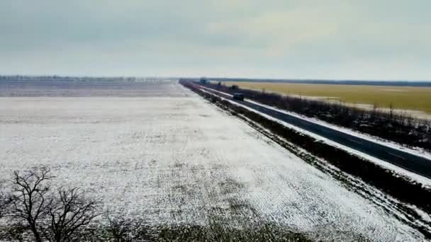 Luftaufnahme Landschaft Landschaft mit schweren LKW bewegt sich durch Asphaltstraße durch Winterfeld mit Wind und Schneefall — Stockvideo