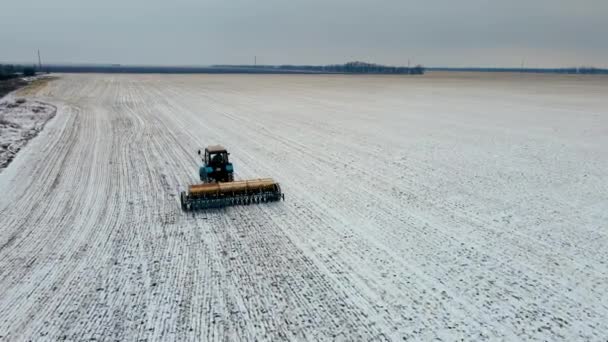 Fermier pe tractor cu unitate agronomică cultivă câmp în timpul iernii și adaugă îngrășăminte în sol înzăpezit — Videoclip de stoc