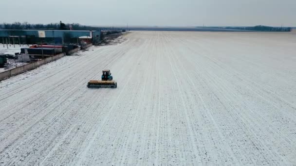 Fertiliser le sol et se préparer au printemps en utilisant un tracteur travaillant sur un champ agronomique avec une couche de neige en hiver près d'une grande ferme rurale — Video