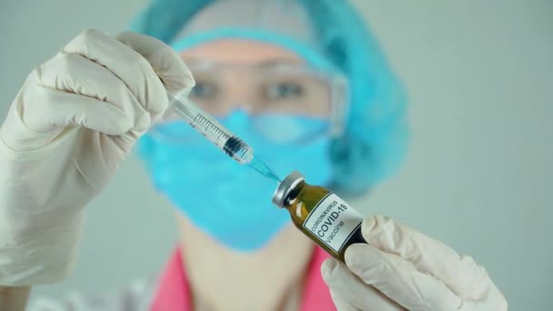 Söt kvinna läkare i skyddshandskar mask och glasögon ringer anti coronavirus vaccin i sprutan från flaskan på sjukhuset — Stockvideo