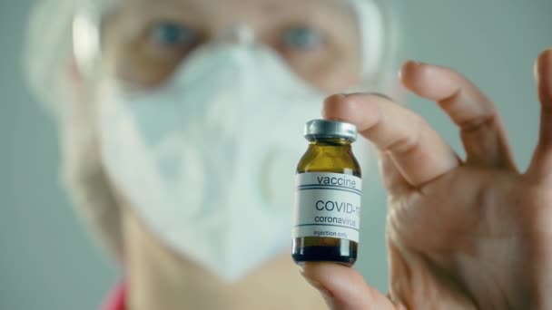 Zavřete lékaře v ochranné masce držící ampulku nebo lahvičku s vakcínou proti koronaviru moderna během celosvětové epidemie — Stock video