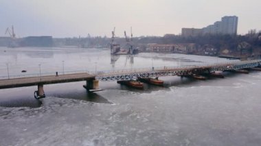 Limandaki yaya köprüsü, büyük yük vinçleri ve nehir boyunca eriyen buzlarla inşa edilen tekne ve gemi iskelesi.