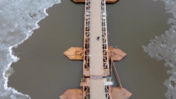 Ponte pedonale in acciaio del pontone con lanterne attraverso il fiume con ghiaccio che si scioglie in inverno e l'uomo solitario che cammina da esso — Video Stock