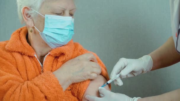 Medical nurse in safety gloves and protective mask making vaccine injection to elderly female patient in health clinic — Stock Video