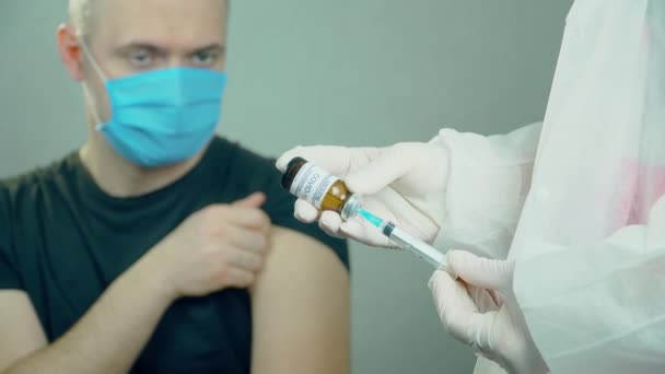 Las manos y jeringas médicas con agujas están listas para vacunar a los pacientes en el laboratorio sobre el fondo de los hombres que usan máscara anticoronavirus azul. — Vídeo de stock