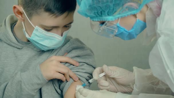 Infirmière médicale en gants de sécurité et masque protecteur faisant l'injection de vaccin au patient garçon dans une clinique de santé — Video
