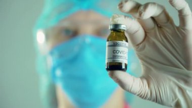 Doktor mikrobiyolog virüs araştırmacısı koruyucu maske ve eldivenlerle laboratuvarda aşı enjeksiyonu ile ampul tutuyor.