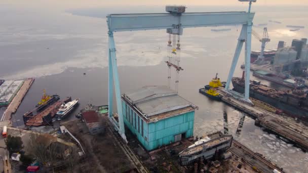 Panorama aéreo sobre enormes grúas utilizadas en astilleros para trabajos de construcción y mantenimiento con graneros metálicos en puerto internacional y yate amarrado en agua con hielo fundido — Vídeos de Stock