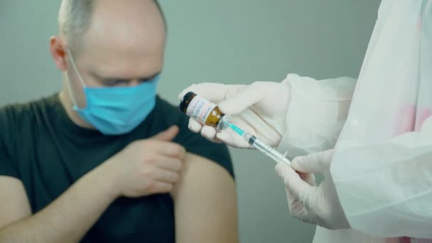Zdravotnické vakcinační zařízení s injekční stříkačkou s jehlou a ampulkou v ruce lékaře nebo zdravotní sestry na pozadí mužského pacienta ze skupiny rizik v nemocnici — Stock video