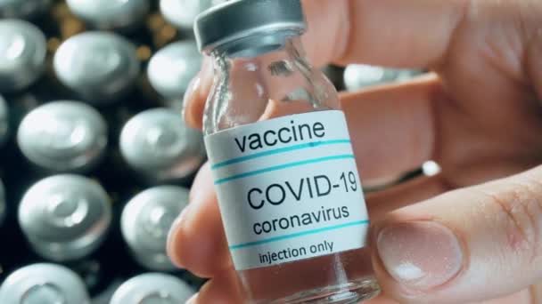 Woman hand holding coronavirus vaccine in bottle on pharmacology drugs in vials background against worldwide pandemic — Stock Video