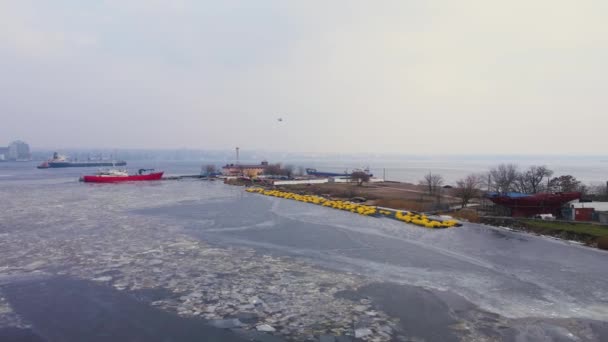 Vue aérienne d'un hélicoptère survolant un quai avec peu de cargos debout sur l'eau avec de la glace fondante et des floes — Video