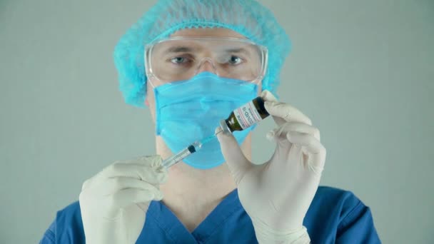 Mężczyzna lekarz w rękawiczkach ochronnych i okularach wybiera szczepionkę przeciw koronawirusowi w strzykawce z butelki w centrum usług medycznych — Wideo stockowe