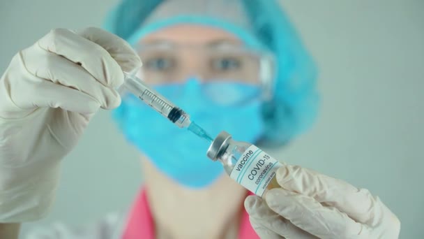 Piękna kobieta lekarz w rękawiczkach ochronnych i okularach wybiera szczepionkę przeciw koronawirusowi w strzykawce z butelki w centrum usług medycznych — Wideo stockowe
