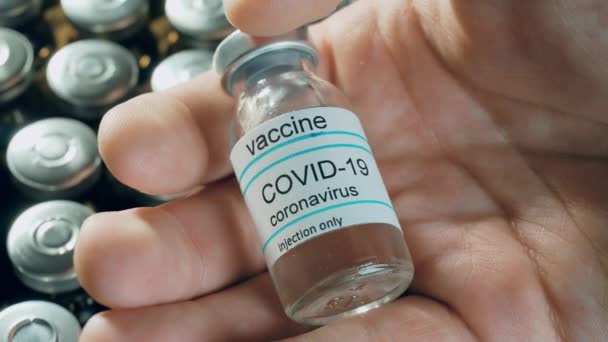 Чоловік тримає вакцину проти коронавірусу в пляшці на фармакологічних препаратах у флаконах на тлі пандемії у всьому світі — стокове відео
