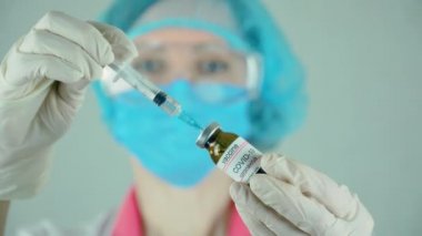 Doktor mikrobiyolog virüs araştırmacısı koruyucu maske ve eldivenler içinde aşı enjeksiyonu ve şırıngayla ampul tutuyor.