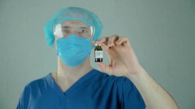 Koruyucu eldivenli bir portre doktoru ve elinde aşı ampulü taşıyor.