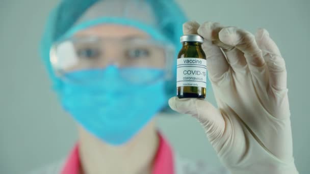 Mujer bonita doctora en guantes de máscara protectora y gafas que sostienen la botella de vacuna contra el coronavirus en el centro de servicios médicos — Vídeos de Stock