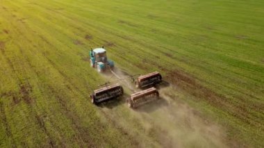 Özel karavan ünitesine sahip güçlü tarım traktörü gün batımında buğday tarlasına mineral ve nitrojen gübresi sür.