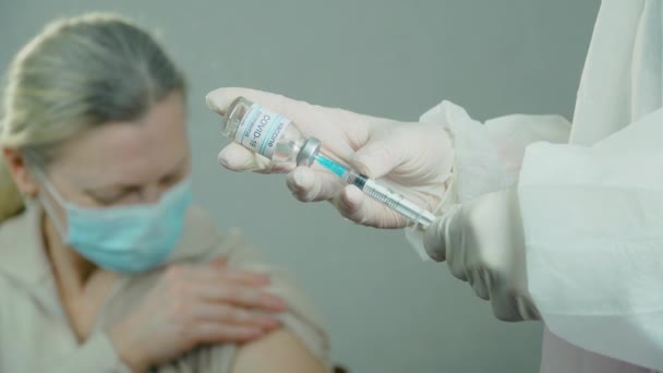 Il medico da vicino conduce ricerche, riempie a mano la siringa con il vaccino coronavirus sullo sfondo della paziente in ospedale — Video Stock