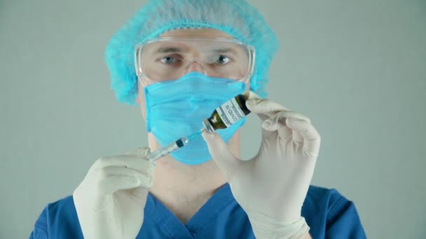 Врач в защитной маске и очках набирает антикоронавирусную вакцину в шприц из бутылки в больнице — стоковое видео