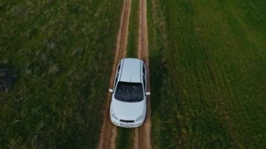 Beyaz küçük hatchback, şehrin çok ilerisindeki ilkbaharda gün batımında tarımsal buğday tarlaları ve arpa tarlaları arasında yol boyunca gidiyor.