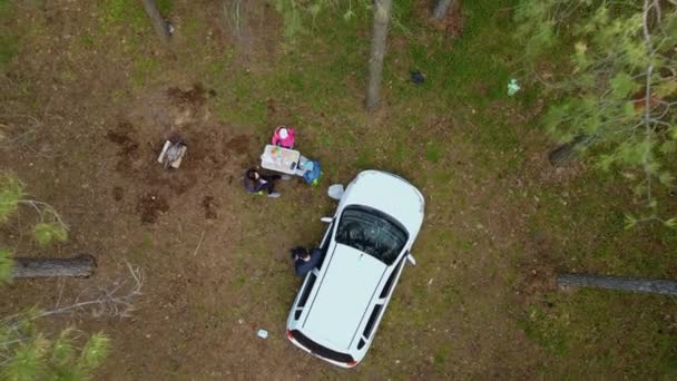 Drone rodaje aéreo cinematográfico se eleva sobre el padre con la madre y los niños descansando en acampar en la naturaleza durante el autoaislamiento entre los pinos altos en el bosque de coníferas a principios de la primavera — Vídeos de Stock