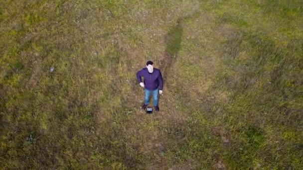 Drone stiger högt över unga kaukasiska mannen står på naturen nära barrskog med tallar och grönt gräs på våren — Stockvideo