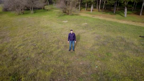 Aerial - flying above young man standing near coniferous forest with pines at sunset — Stock Video