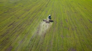 Gübreler için karavanı olan tarım traktörü kırsal alanda sürüş yapıyor ve ilkbaharda buğday ekinlerine kimyasallar ekiyor.