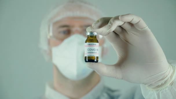 Male researcher in protective sterile wear holding medical tube with samples of anti coronavirus vaccine for injection in laboratory — Stock Video